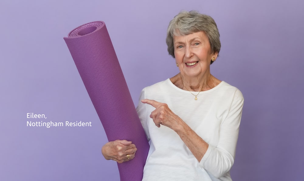 Eileen, Nottingham resident holding and pointing to purple yoga mat