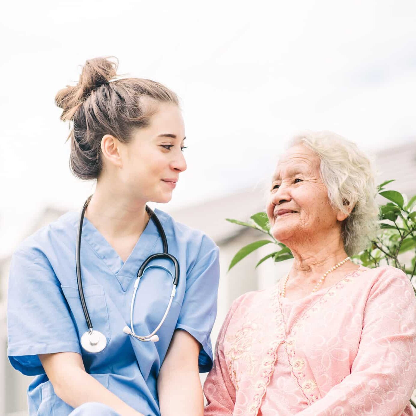 Smiling nurse caregiver holding hand of happy Asian elderly woman outdoor in the park